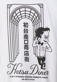 Homme en dessin animé avec un nœud papillon près d'un portail noir et blanc en arc avec du texte japonais et l'adresse "Hatsu Diner" à Shibuya, Tokyo.