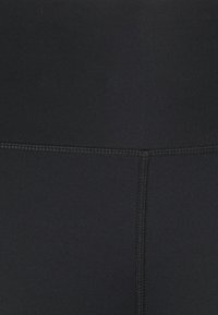 Czarne legginsy sportowe z gładkiego materiału, wysokim pasem i widocznym płaskim szwem, oferujące dopasowany krój i elastyczną teksturę.