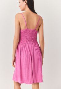 Lyserød sommerkjole med justerbare tynde stropper, rynket overdel og en flydende nederdel. Fremstillet af let stof med en tekstureret finish.