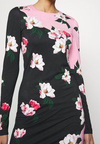 Robe à manches longues avec une base noire, des sections roses et des motifs floraux blancs. Le tissu est lisse et présente une silhouette ajustée.