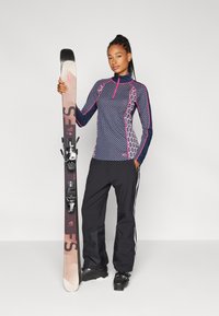 Sporty skiklær som har en mønstret marineblå og rosa topp, svarte skibukser med hvite striper, og ski med svarte bindinger.