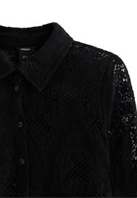 Svart spets skjorta med knappar som har krage, texturerat mönster och tonala knappar. Tyget har en intrikat öppningsdesign.