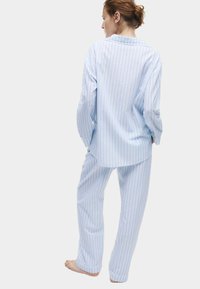 Lichtblauw en wit gestreept pyjamapakket, met een lange mouwen knoopsluiting top en loszittende broeken. Katoenen materiaal met een zachte textuur.