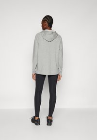 En heathergrå hoodie med dragsko och långa ärmar, ihopparad med svarta leggings och svarta skor, sedd bakifrån.