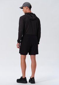 Svarta idrottshorts i kombination med en långärmad, mörkgrå huvtröja. Har en huva, elastisk midja och löparskor. Minimalistisk design.