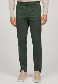 Gröna chinos i bomull med rak bendesign, framfickor och en mjuk textur. Bärs med ljusbeige sneakers.