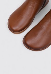 Brown leather slip-on boots with a smooth, rounded toe, textured upper, and a subtle seam detail along the edges.