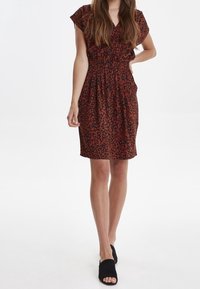 Leopardmönstrad klänning i rödbrunt tyg, korta ärmar, rynkad midja, svajande kjol, kombinerad med svarta slip-on-skor.