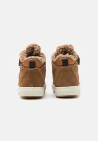Brune suéde ankelstøvler med en fluffy beige foret, hvide gummisåler og kontrasterende sorte stofdetaljer ved hælen og tungen.