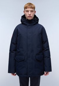 Parka isolata di colore blu navy con colletto alto e cappuccio regolabile, dotata di due tasche anteriori a toppa e di un logo sulla manica.