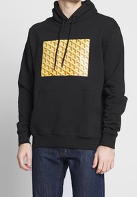 Black hoodie with front pocket, featuring a rectangular yellow and red geometric pattern design. Made of soft fabric with a drawstring hood.