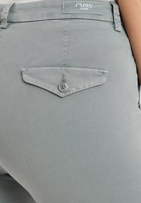 Graue Baumwollhosen haben eine Gesäßtasche mit einer spitzen Klappe und einem einzigen Knopf. Ein Etikett mit "CMRV" ist am Bund angenäht.