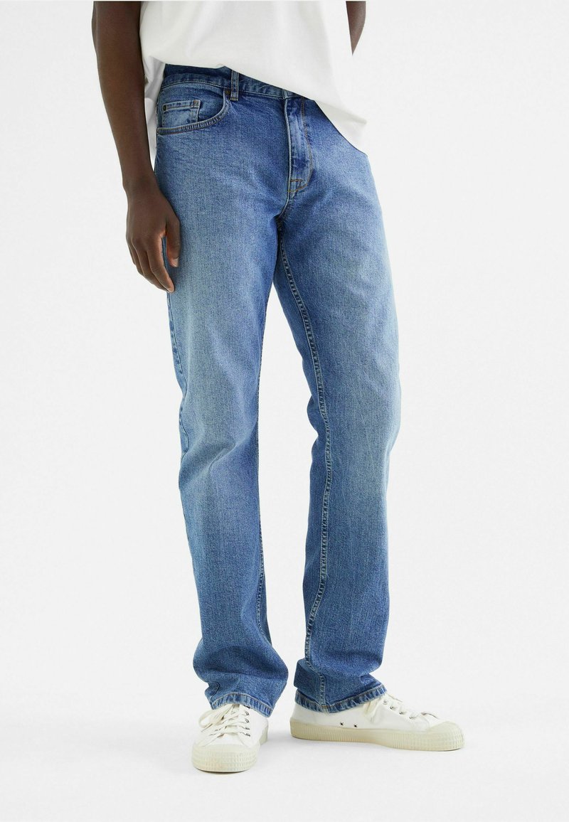 Blauwe denim jeans met een rechte snit, voorzien van een voorzak, subtiele vervaging en gecombineerd met witte sneakers.