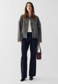 Sivá vlnená bunda s okrúhlym výstrihom, zapínaním na gombíky a spustenými ramenami. Kombinovaná s džínami s vysokým pásom a bordovou taškou.