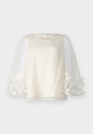 White top featuring a smooth fabric with dotted texture, sheer puff sleeves adorned with flower appliqués, and round neckline.