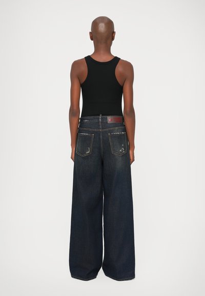 Jeans de denim de pierna ancha en azul oscuro con detalles desgastados, combinados con una camiseta negra ajustada, vistos desde atrás.