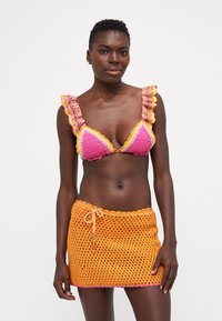 Bikini de ganchillo colorido con copas triangulares en rosa y naranja, con tirantes con volantes; combinado con una falda de ganchillo naranja a juego.