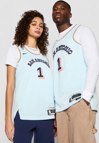 Šviesiai mėlyni krepšinio marškiniai su "SAN ANTONIO" ir numeriu "1" tamsiai mėlyna spalva. Su oranžiniais akcentais ir NBA logotipais apatinėje dalyje.