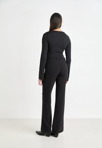 Black long-sleeve top paired with high-waisted black wide-leg pants, featuring a fitted silhouette, smooth fabric, and pointed black shoes.