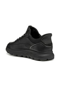 Zapatilla negra de cuero con una suela gruesa negra, puntera redondeada y diseño minimalista. Presenta una textura suave y un branding sutil en el talón.