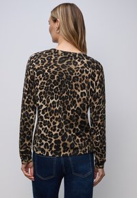 Pullover mit Leopardenmuster in Beige und Schwarz, mit langen Ärmeln, einem Rundhalsausschnitt und weicher Textur, kombiniert mit dunklen Jeans.