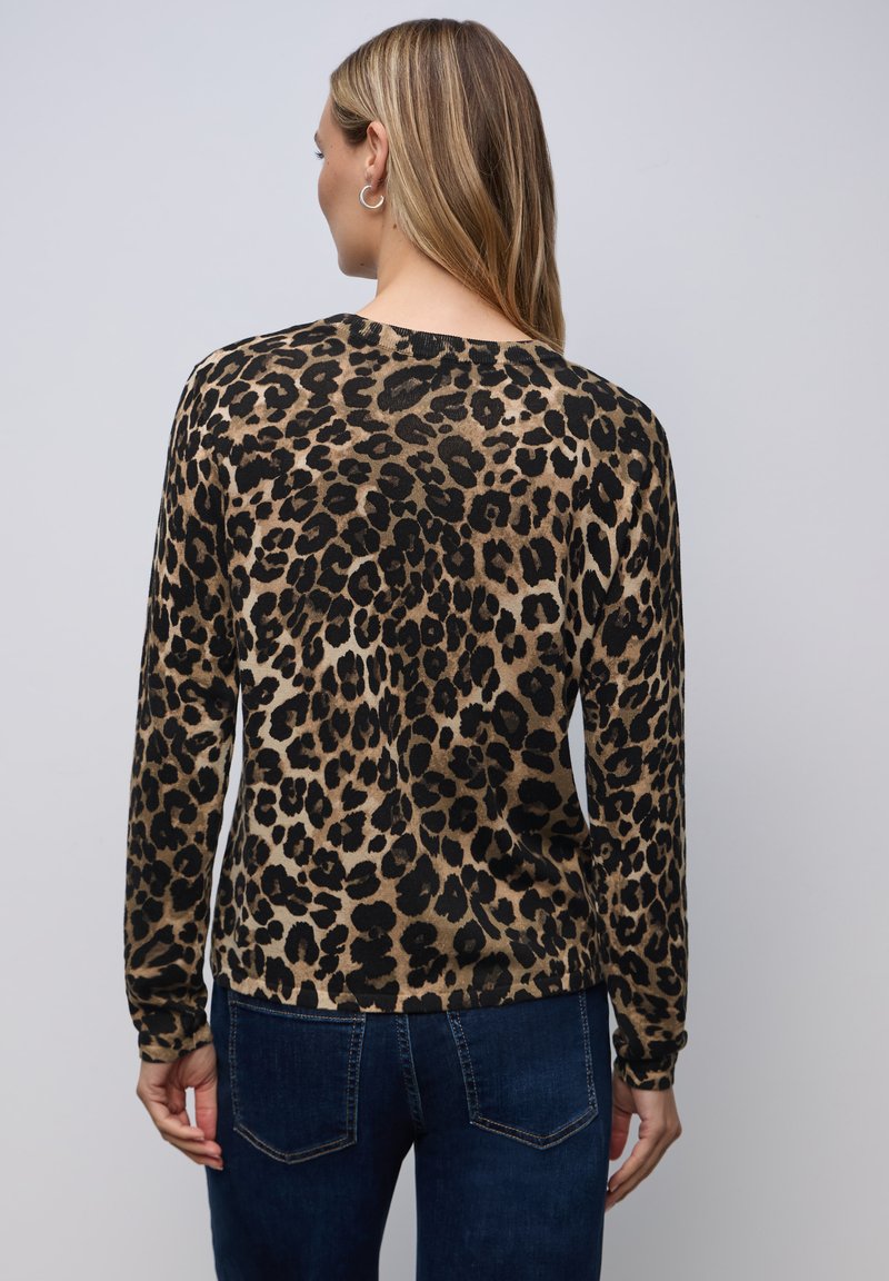 Pullover mit Leopardenmuster in Beige und Schwarz, mit langen Ärmeln, einem Rundhalsausschnitt und weicher Textur, kombiniert mit dunklen Jeans.