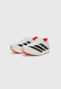 White sneakers with black stripes, neon green and red accents, lightweight design, and a textured sole for grip.