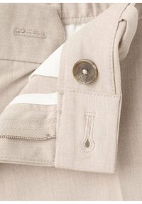 Camisa beige abotonada con tela texturizada, que presenta un botón redondo, detalles blancos en contraste y acentos de costuras visibles.