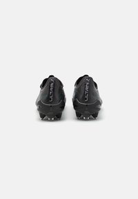 Botas de fútbol sintéticas negras con una superficie texturizada, que presentan un diseño de corte bajo y una destacada marca "ULTRA" en el talón.