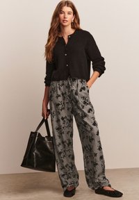 Cardigan noir en maille avec boutons, associé à un pantalon à jambes larges noir et blanc à motifs floraux et à carreaux. Sac à main noir inclus.