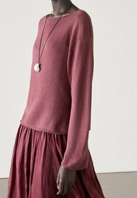 Maglione a collo barca di colore bordeaux, con maniche lunghe e orlo a costine, abbinato a una gonna bordeaux fluida con texture arricciata.