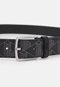 Curea din piele neagră cu model geometric și cataramă din metal argintiu. Are cusături contrastante și un detaliu cu logo pe buclă.