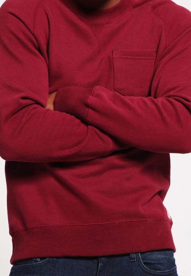 Punainen collegepaita pyöreällä pääntiellä, resorilla hihoissa ja helmassa sekä etutaskulla. Valmistettu pehmeästä kankaasta, jossa on sileä pinta.