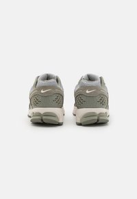 Baskets de sport Nike avec un dessus en maille et en cuir suédé gris et beige, présentant un motif texturé et le logo emblématique sur le talon.