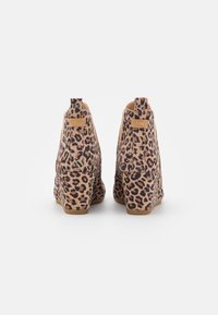 Bottes de cheville à talon compensé en suède à imprimé léopard, avec une base beige, des taches noires et un petit accent doré à l'arrière.