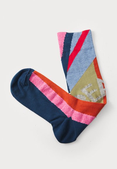 Bunte Socken aus weichem Stoff, mit geometrischen Mustern in Blau, Pink, Orange und Grün, gestricktem Bund und unterschiedlichen Texturen.