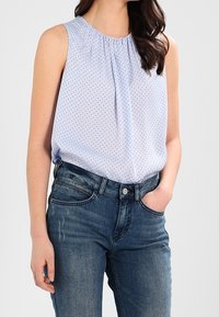 Blouse sans manches bleu clair avec un col froncé et de petits pois noirs, associée à un jean en denim bleu foncé au fit classique.