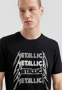 Schwarzes Baumwoll-T-Shirt mit fettem, geschichtetem "METALLICA"-Text in Silber und Blitzakzenten. Klassisches Rundhals-Design.