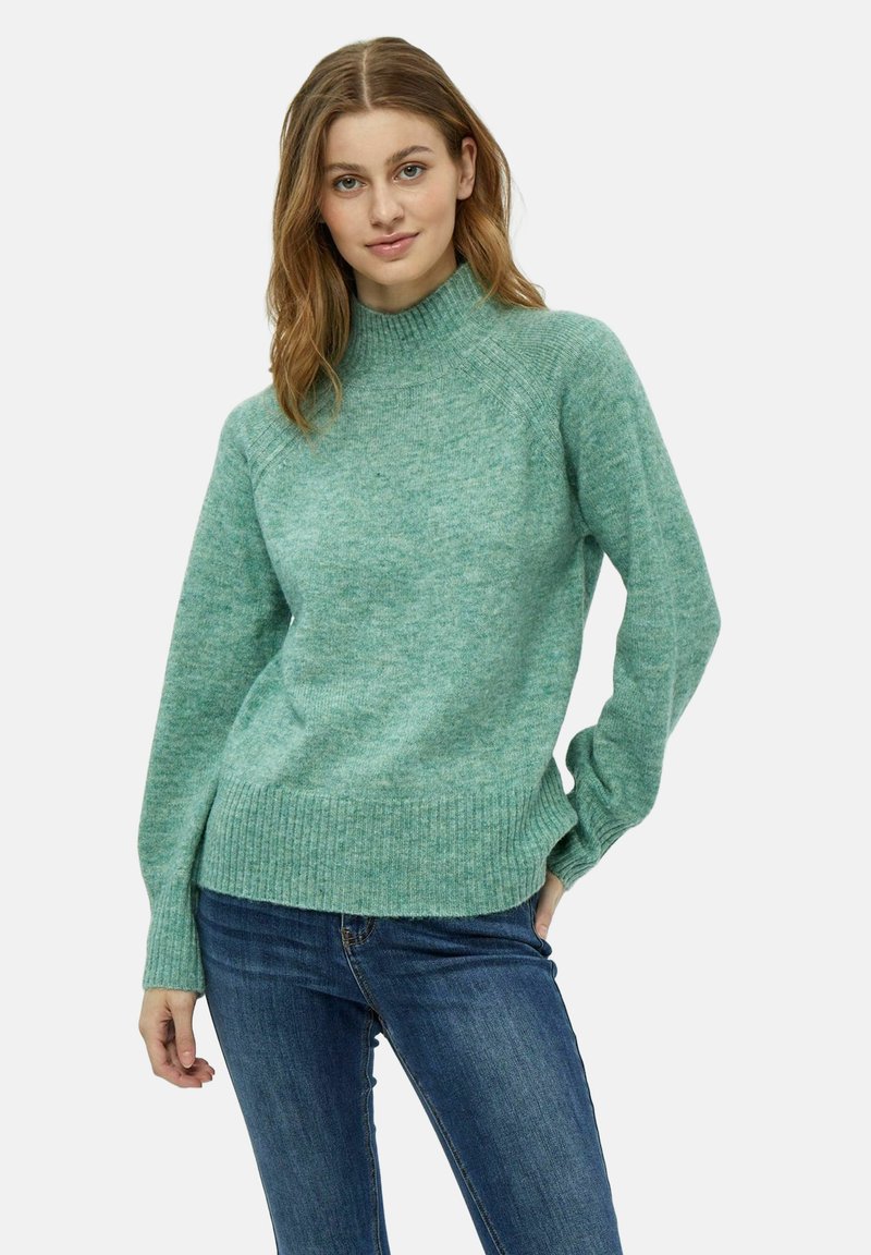 Maglione lavorato a maglia verde menta con collo alto, orlo a coste e maniche lunghe, abbinato a jeans blu scuro. Texture morbida e vestibilità casual.