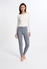 Witte lange mouwen top met een knoopsluiting bij de hals, gecombineerd met grijze nauwsluitende legging, beide gemaakt van zachte, rekbare stof.