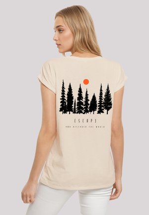 Blonde woman wearing beige shirt with black pine trees, orange sun, and text "ESCAPE and discover the world" on the back.