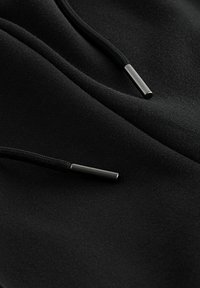 Felpa nera con zip realizzata in tessuto morbido, con estremità in metallo sui lacci e una superficie liscia.