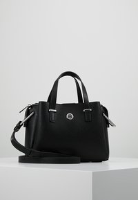 Mustan nahkalaukun, jossa on kaksinkertaiset yläkahvat, irrotettava olkahihna, hopeiset yksityiskohdat ja pyöreä logo etupuolella. Rakeinen pinta.