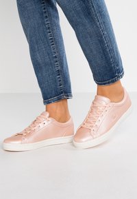 Baskets en cuir rose clair avec lacets plats, bout rond et semelles en caoutchouc blanches. Caractéristiques d'un design minimaliste et logo embossé sur le côté.