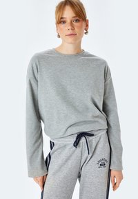 Grauer Langarm-Pullover mit Rundhalsausschnitt, kombiniert mit grauen Jogginghosen mit marineblauen Seitenstreifen und einem Logo. Eignet sich für lässige Outfits.