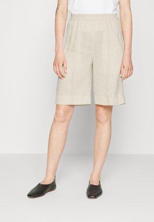 Shorts en lin beige clair avec une taille élastique, coupés au niveau des genoux et avec une finition texturée, associés à des chaussures plates noires.