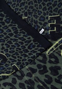 Tissu à imprimé léopard vert et noir avec bordure noire et étiquette blanche étiquetée "CECIL", partiellement plié.
