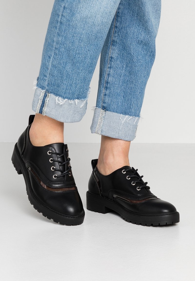 Sorte lædersko med lav hæl og rund tå. Har snørebånd, sideaccenter og en tekstureret sål. Rulled cuff denim er synlig.