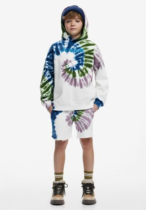Tie-dye hoodie and shorts set in white, featuring blue, green, and purple spirals. Worn with beige boots and striped green and gold socks.