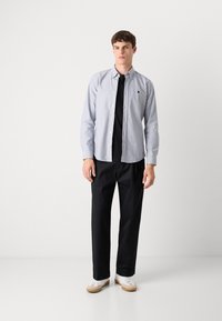 Lichtblauw overhemd met knopen, gedragen over een zwart T-shirt, gecombineerd met zwarte broeken en witte sneakers met beige accenten. Eenvoudig ontwerp en pasvorm.